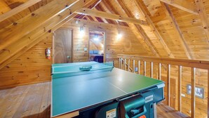 A ping pong table in a wooden room with a sloped ceiling and a wooden railing.