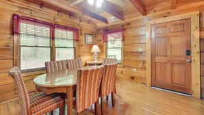 A wooden cabin interior with a dining table, chairs, a ceiling fan, and a large wooden door.