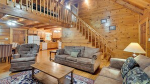 A spacious living area with a wooden staircase, a sofa set, a coffee table, and a rug.