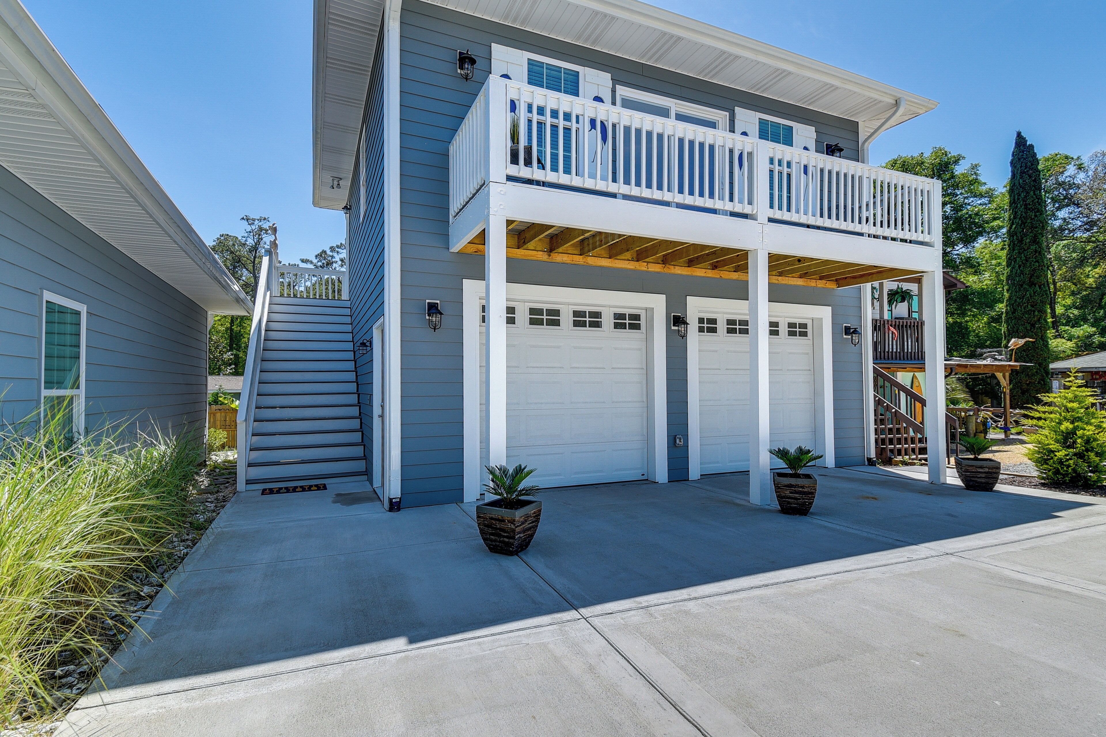 A two-story house with a balcony, two garage doors, and potted plants.