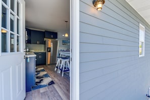 A modern kitchen with dark cabinets, a refrigerator, and a dining area with a table and chairs. - 1 Mi to Beach & Pier! Chic Ocean Isle Studio (Ocean Isle Beach)