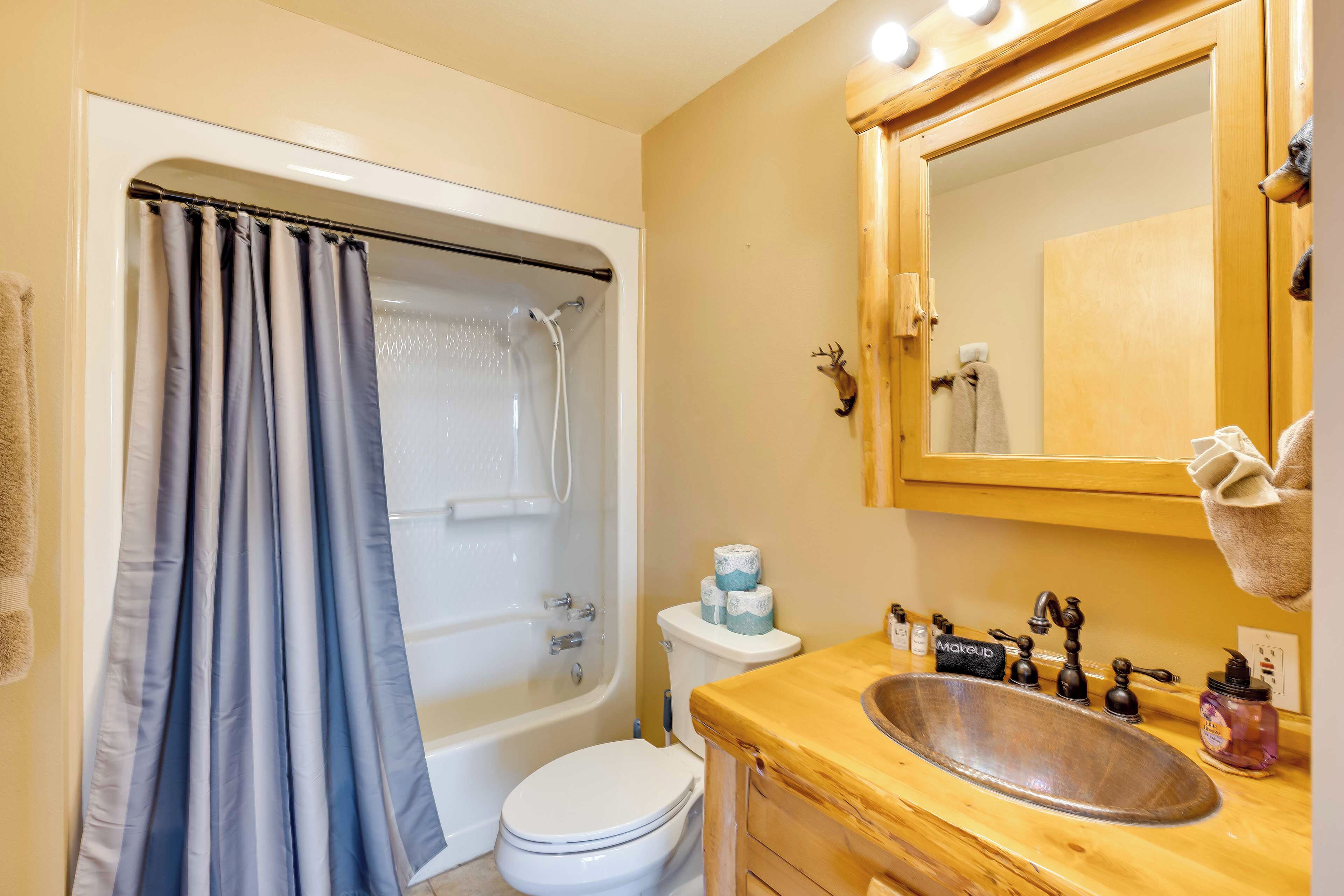 A bathroom with a bathtub, toilet, wooden vanity, sink, and a mirror.