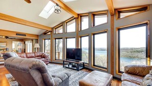 A spacious living room with a large TV, leather sofas, and a view of a lake.