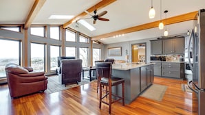 A spacious kitchen with wooden floors, large windows, and a ceiling fan.