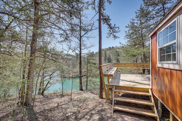 A cabin with a wooden deck overlooking a lake, surrounded by trees.