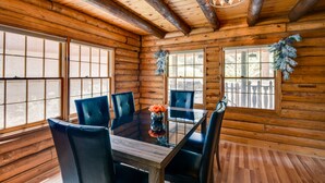 A wooden cabin interior with a dining table, chairs, large windows, and a chandelier. - Pine Mountain Club Cabin w/ Community Pool! (Pine Mountain Club)
