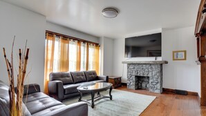 A living room with a leather sofa, a glass coffee table, a stone fireplace, and a flat-screen TV mounted above it. - Buffalo Vacation Rental ~ 20 Mi to Niagara Falls! (Buffalo)