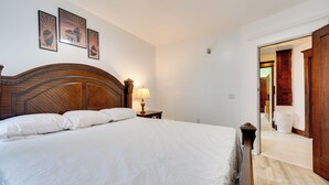 A neatly made bed with white linens, a wooden headboard, and a bedside table with a lamp. There are three framed pictures on the wall above the bed. - Buffalo Vacation Rental ~ 20 Mi to Niagara Falls! (Buffalo)