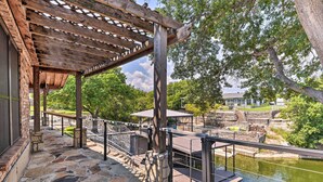 A stone-paved deck with a wooden pergola, stone walls, and a view of a river. - Luxury Granbury Home w/ Private Boat Dock! (Granbury)