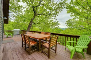 A wooden deck with a table and chairs, a grill, and a green Adirondack chair. - Secluded Cabin w/ Hot Tub Near Table Rock Lake! (Kimberling City)
