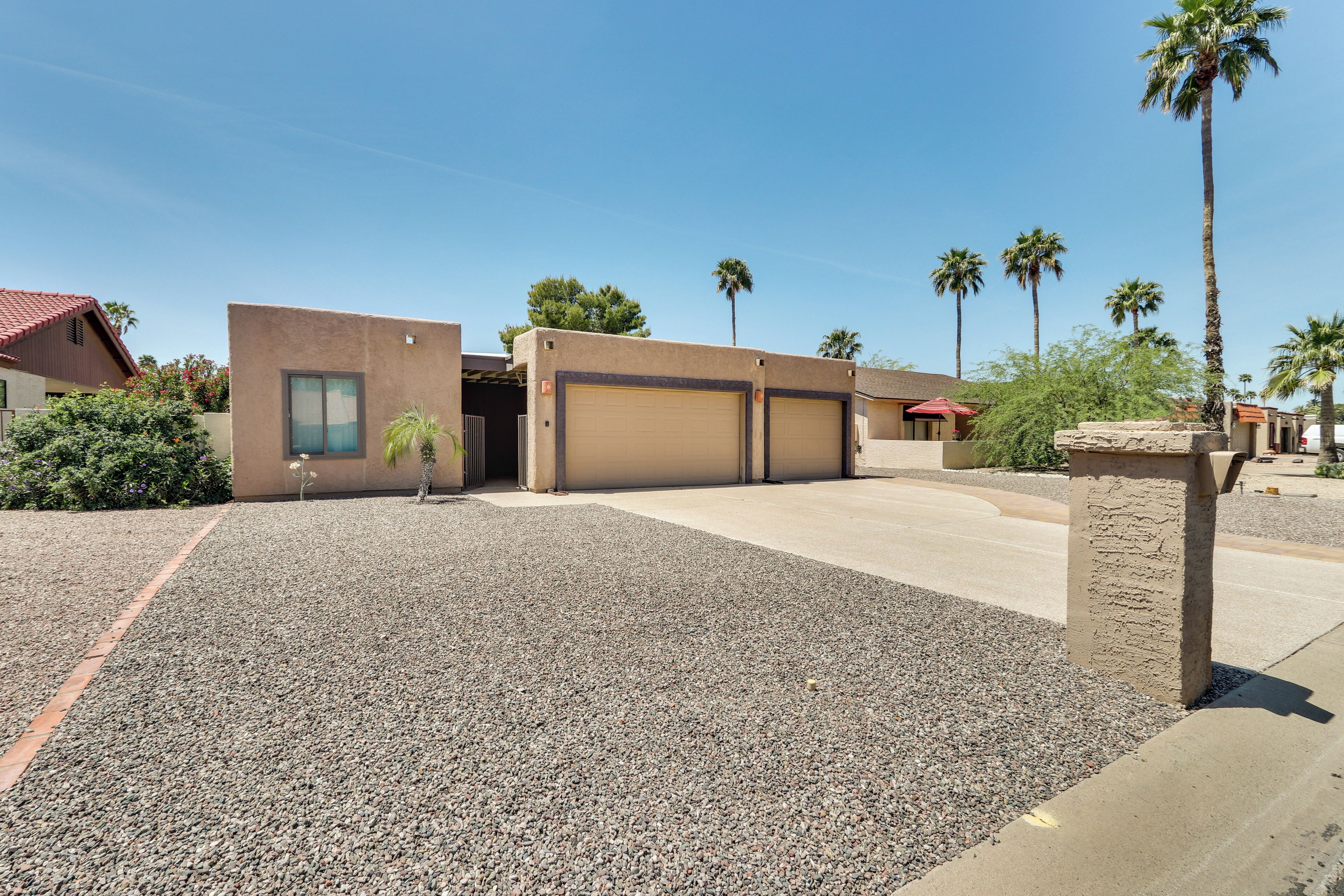 A residential area with a house featuring a garage, a gravel driveway, and palm trees.