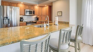 A kitchen with granite countertops, stainless steel appliances, wooden cabinets, and two bar stools. - Waterfront Nokomis Condo < Half Mile to Beach! (Nokomis)