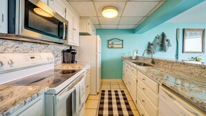 Une cuisine avec des meubles blancs, un four à micro-ondes, une cuisinière et un tapis de sol à carreaux.