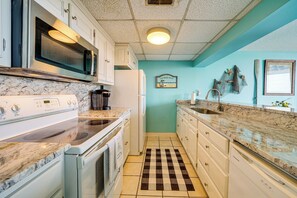 Une cuisine avec des meubles blancs, un four à micro-ondes, une cuisinière et un tapis de sol à carreaux.
