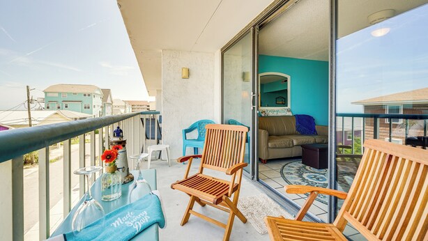 Un balcon avec une chaise en bois, une table en verre sur laquelle est posée une serviette, et une vue sur l’intérieur d’une maison.