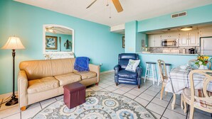 Un salon avec un canapé beige, un fauteuil bleu, une table basse et un tapis à motifs.
