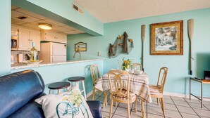 Une cuisine avec des meubles blancs, un réfrigérateur et un coin repas comprenant une table et des chaises.