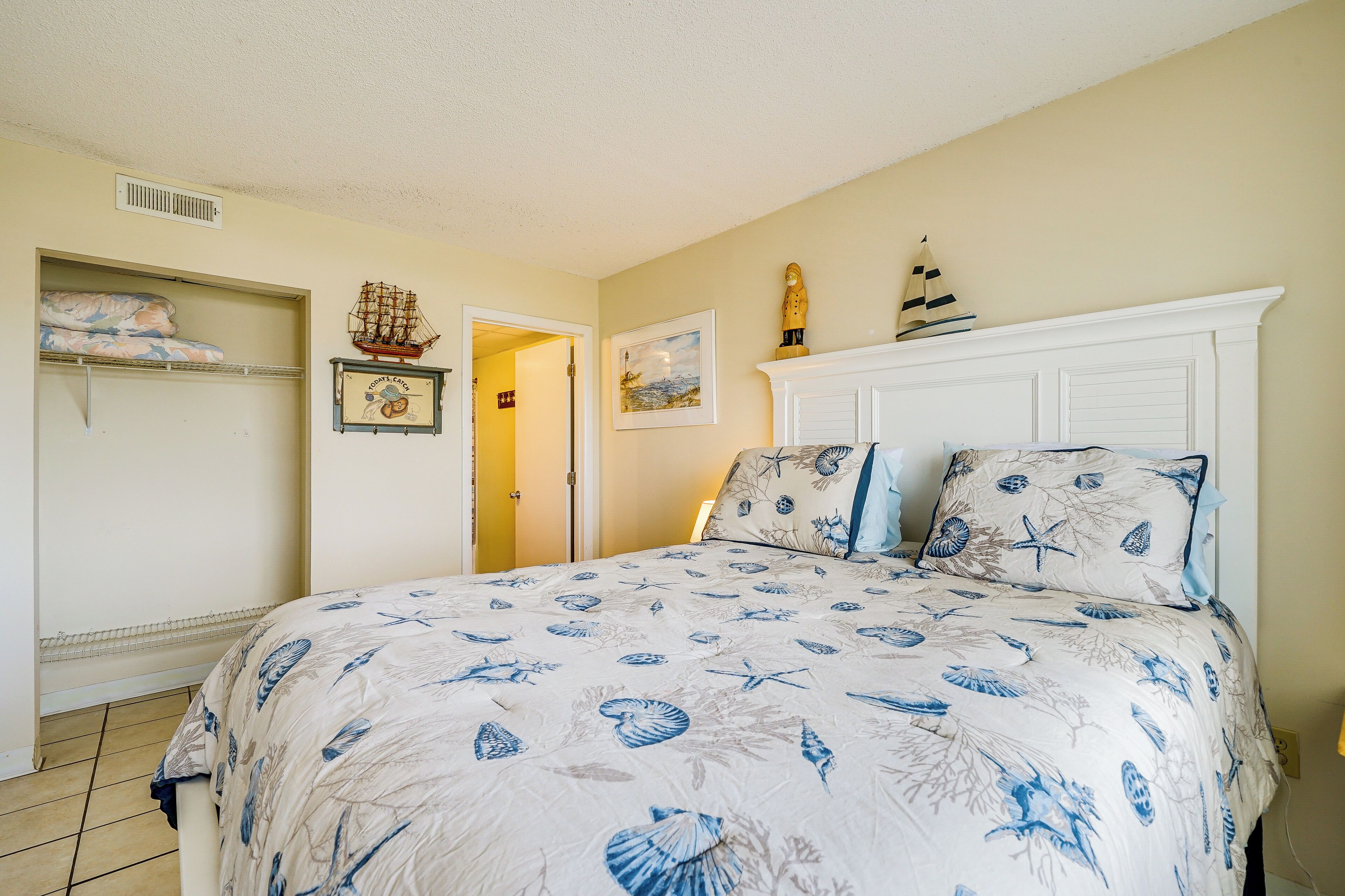 Une chambre à coucher avec un lit, une étagère où sont pliées des serviettes, une maquette de bateau et un tableau accroché au mur.