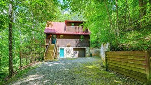 A two-story cabin with a stone facade, a red roof, and a gravel driveway leading to a wooden gate. - Mountain-view Robbinsville Cabin w/ Hot Tub! (Robbinsville)