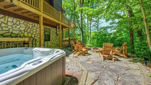 A hot tub on a stone patio with wooden chairs and a stone wall. - Mountain-view Robbinsville Cabin w/ Hot Tub! (Robbinsville)