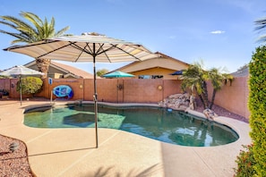 A swimming pool with a curved edge, surrounded by a brick wall and palm trees.