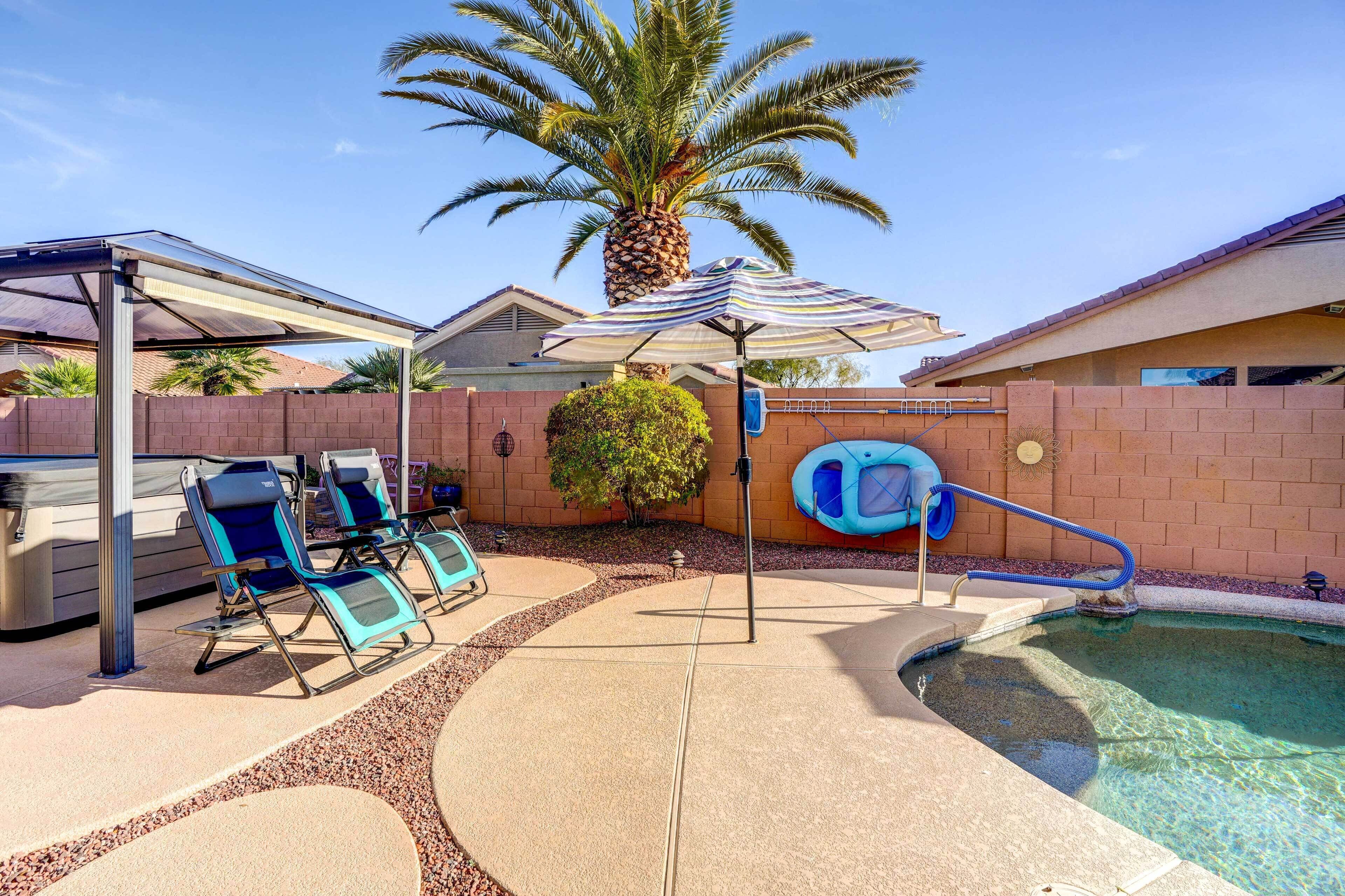 A backyard with a swimming pool, lounge chairs, a palm tree, and a covered patio area.