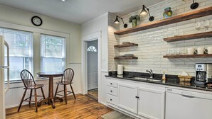 Une cuisine avec des meubles blancs, un plancher en bois, une table à manger avec des chaises et une horloge au mur.