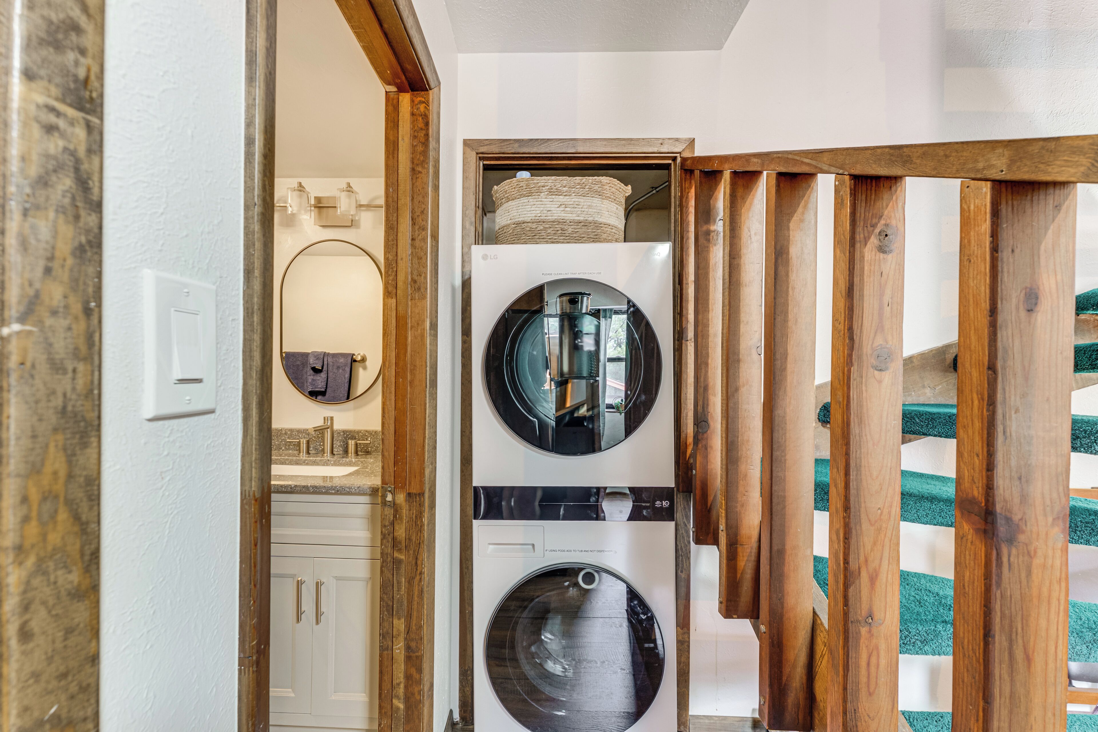 A laundry room with two stacked front-loading washing machines, a wooden-framed door, and a mirror above the sink.
