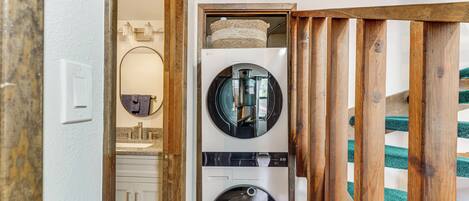 A laundry room with two stacked front-loading washing machines, a wooden-framed door, and a mirror above the sink.