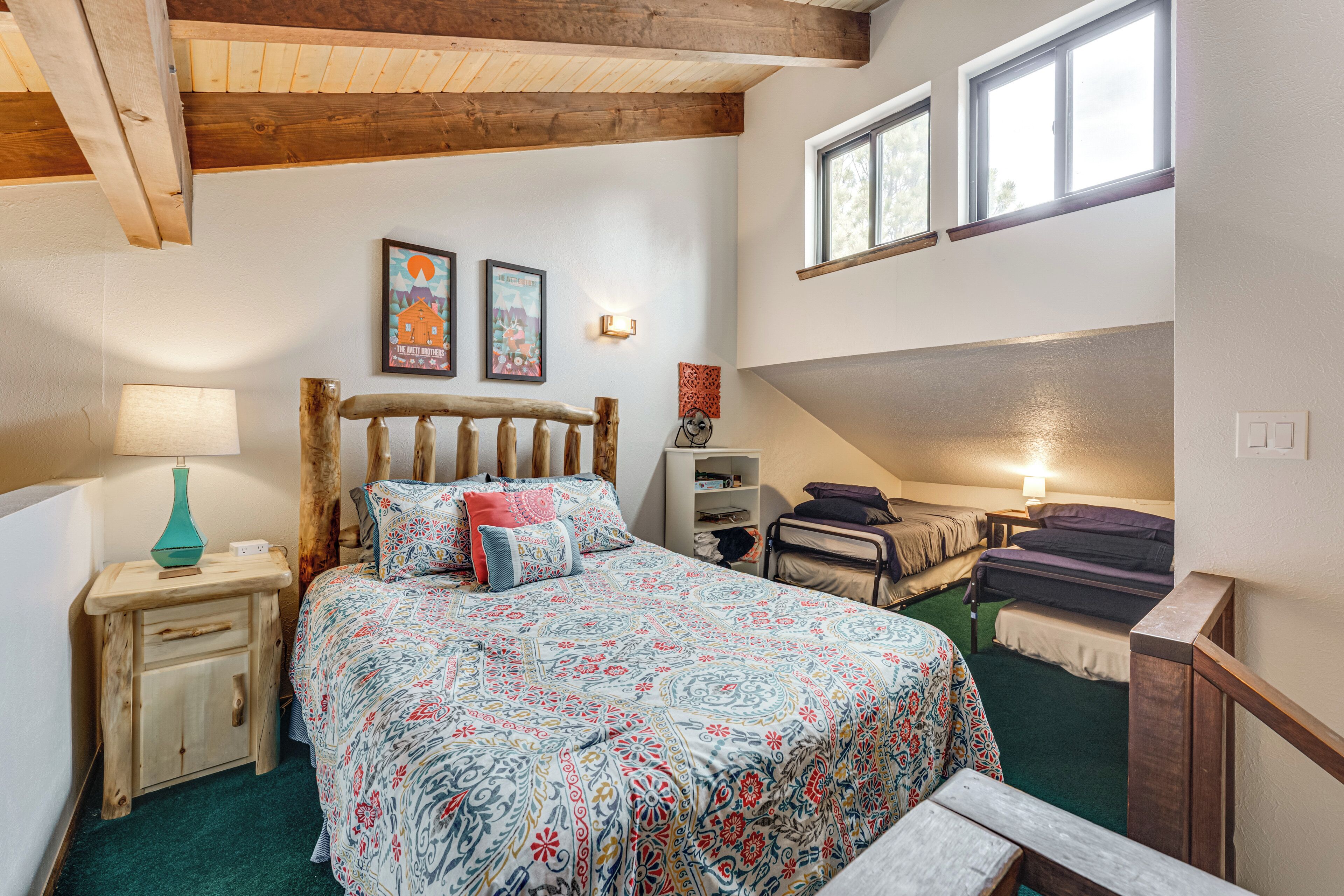 A bedroom with a large bed, a bedside table with a lamp, a wooden headboard, and two framed pictures on the wall.
