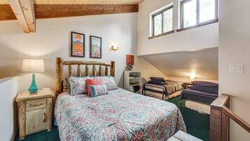 A bedroom with a large bed, a bedside table with a lamp, a wooden headboard, and two framed pictures on the wall.