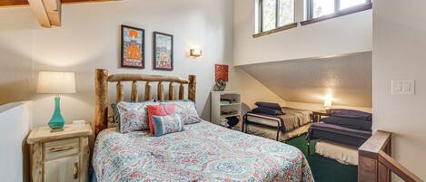 A bedroom with a large bed, a bedside table with a lamp, a wooden headboard, and two framed pictures on the wall.