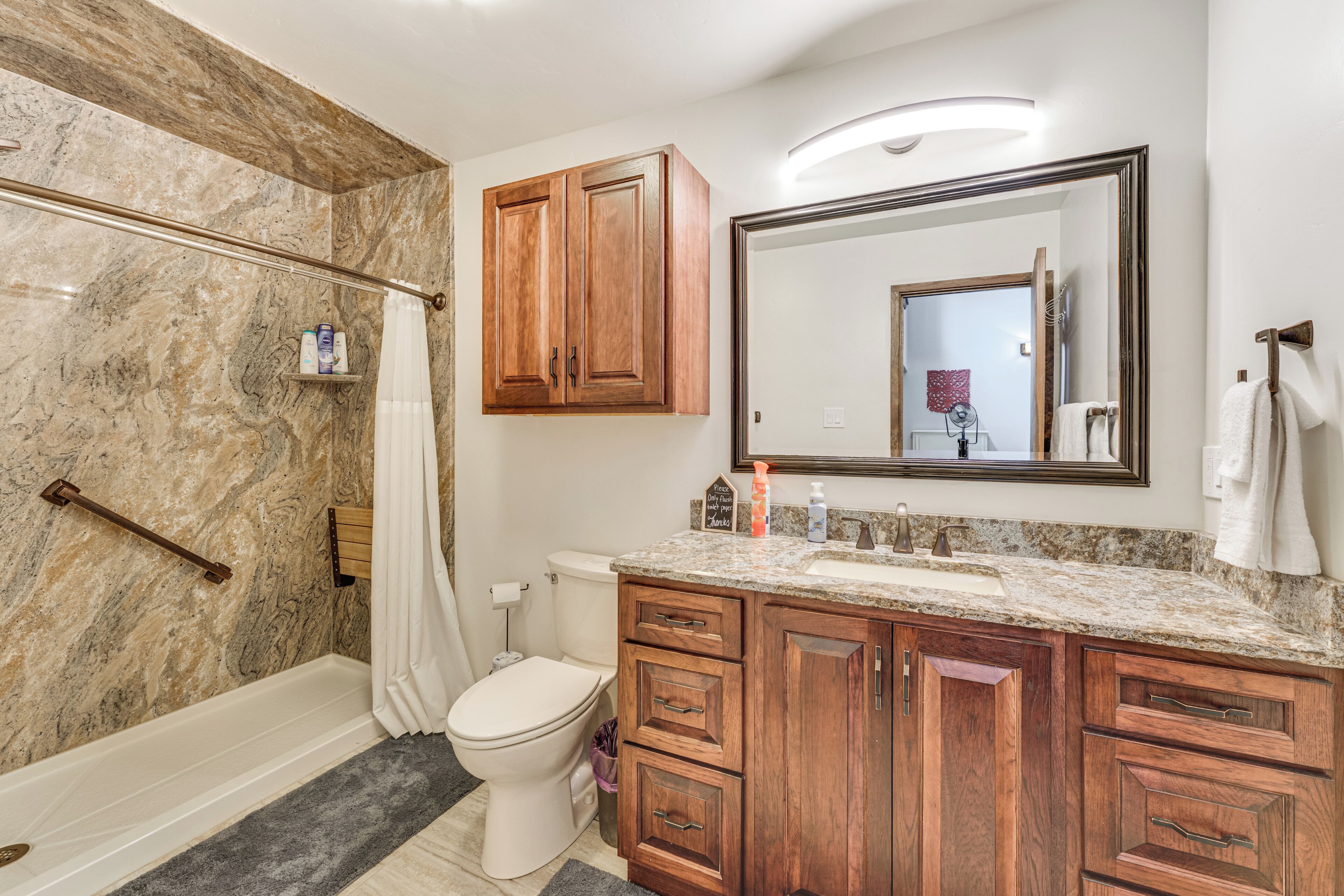 A bathroom with a shower, toilet, vanity with drawers, and a large mirror.