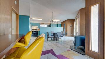 A modern kitchen with a dining area, a yellow sofa, and a patterned rug.