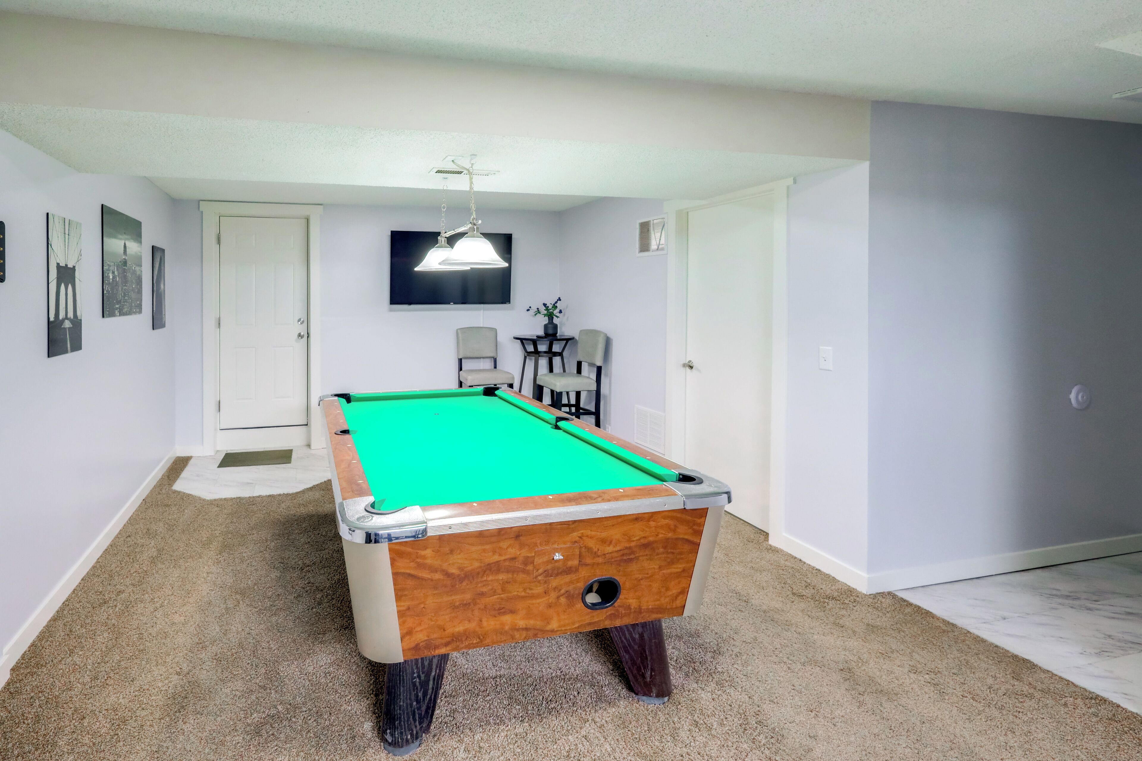 A pool table in a room with a carpeted floor, a door, and a wall-mounted TV.