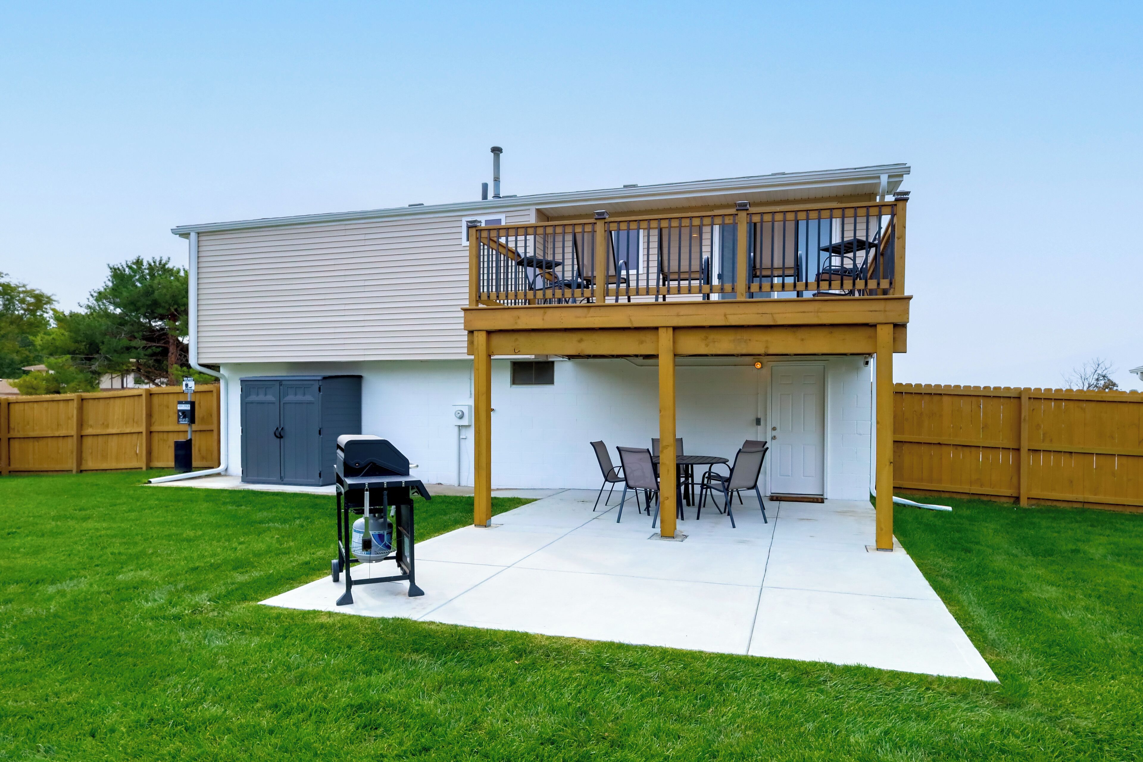 A two-story house with a covered patio area, a barbecue grill, and a fenced backyard.