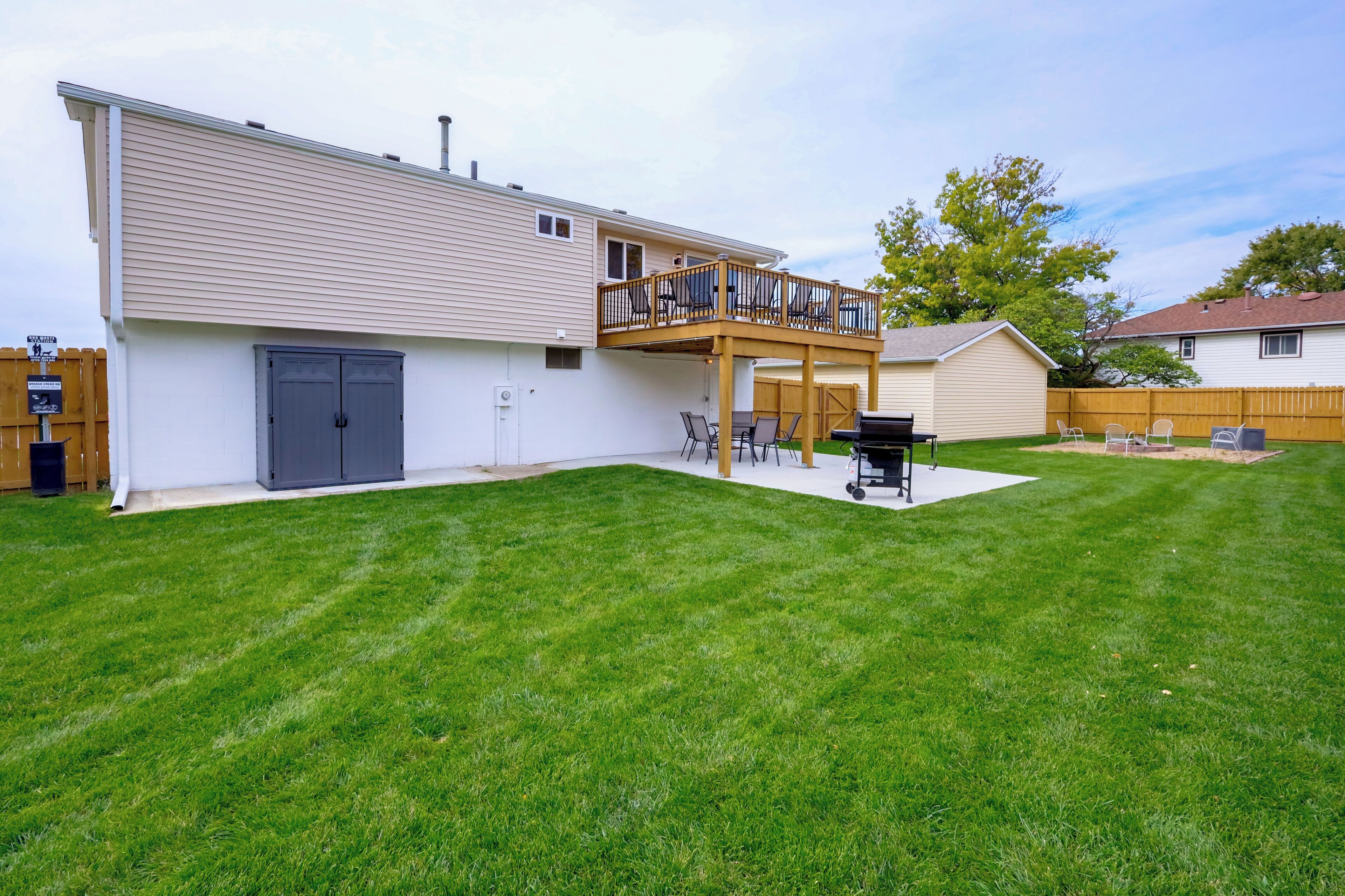 Ein zweistöckiges Haus mit einer Terrasse, einer überdachten Veranda und einem Garten mit Rasen und Grillplatz.