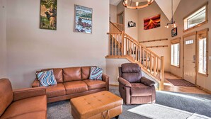 A living room with a brown leather sofa, a brown leather armchair, and a brown ottoman. There is a staircase with wooden railings leading to a door. - Family-friendly Oregon Vacation Home w/ Yard (Bend)