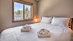 A bedroom with a large bed, two pillows, a bedside lamp, and a window with a view of trees. - Family-friendly Oregon Vacation Home w/ Yard (Bend)