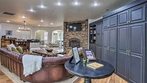 A spacious living room with a stone fireplace, leather sofa, and a round table with a welcome sign. - Beautiful Ranch Home w/ Cascade Mountain View (Powell Butte)