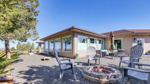A house with a patio area featuring Adirondack chairs, a fire pit, and a view of the surrounding landscape. - Beautiful Ranch Home w/ Cascade Mountain View (Powell Butte)