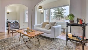 A living room with a white sofa, a wooden coffee table, a patterned rug, and a black console table with books and a lamp. - Beautiful Ranch Home w/ Cascade Mountain View (Powell Butte)