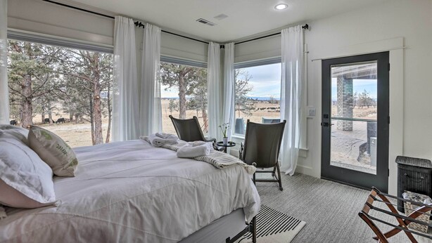 A bedroom with a large bed, two chairs, a small table, and a view of trees and a distant landscape. - Beautiful Ranch Home w/ Cascade Mountain View (Powell Butte)