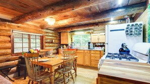 A rustic cabin interior with a wooden dining table, chairs, a kitchen area with a stove, and a refrigerator. - Cozy Elizabethtown Cabin w/ Fire Pit! (Elizabethtown)