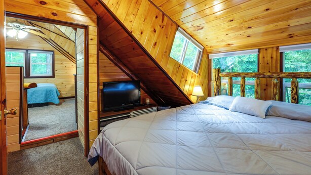 A wooden cabin bedroom with a bed, a television, and a window overlooking greenery. - Cozy Elizabethtown Cabin w/ Fire Pit! (Elizabethtown)