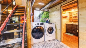 A laundry area with two washing machines, a wooden staircase, and a view of a mountain through a window. - Cozy Elizabethtown Cabin w/ Fire Pit! (Elizabethtown)