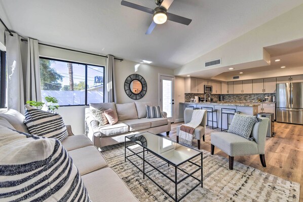 A modern living room with a sofa, armchairs, a coffee table, and a kitchen in the background.