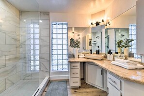 A modern bathroom with a large mirror, a glass shower enclosure, and a vanity with a sink and countertop.