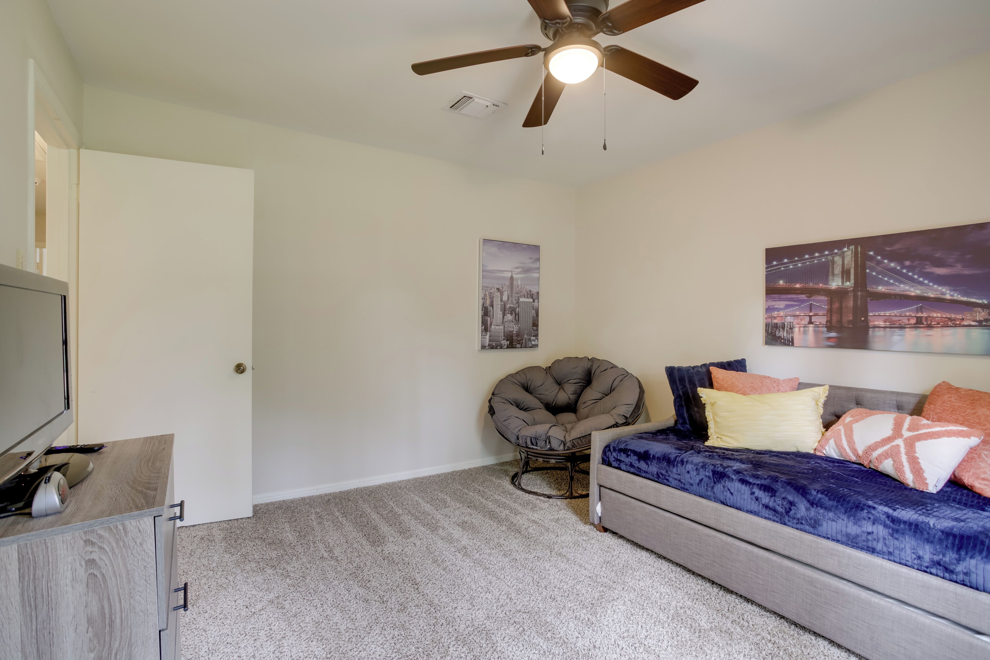 A bedroom with a bed, a chair, a TV, and a ceiling fan.