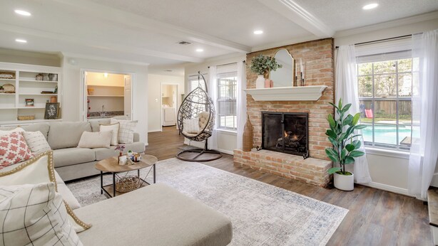 A spacious living room with a fireplace, a hanging chair, and a view of a pool through large windows.
